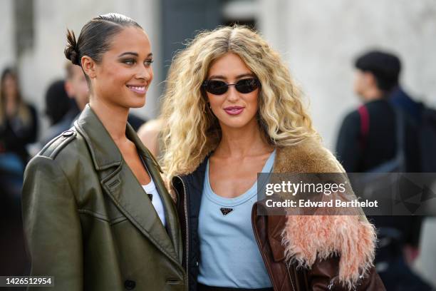 Sarah Lysander wears a white tank-top from Prada, a khaki shiny leather oversized jacket from Prada, Emili Sindlev wears black sunglasses, gold...