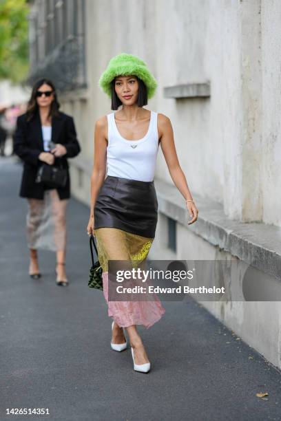 Molly Chiang wears a green fluffy bob hat, a white tank-top from Prada, a multi materials black shiny leather / yellow tulle / pink tulle long skirt...