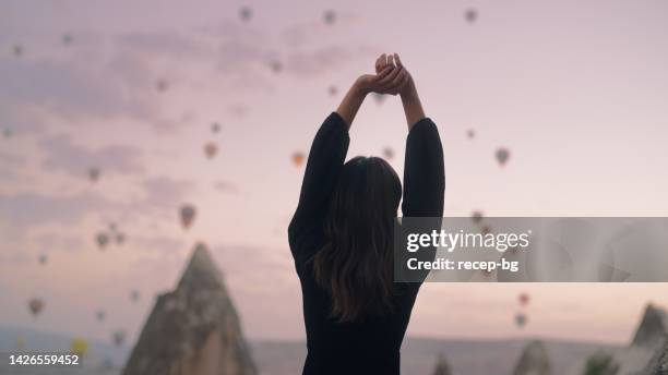 female tourist enjoying watching hot air balloons flying in the sky at rooftop of hotel where she is staying during her vacation - staying in hotel stock pictures, royalty-free photos & images