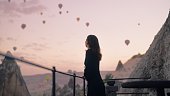 Female tourist enjoying watching hot air balloons flying in the sky at rooftop of hotel where she is staying during her vacation