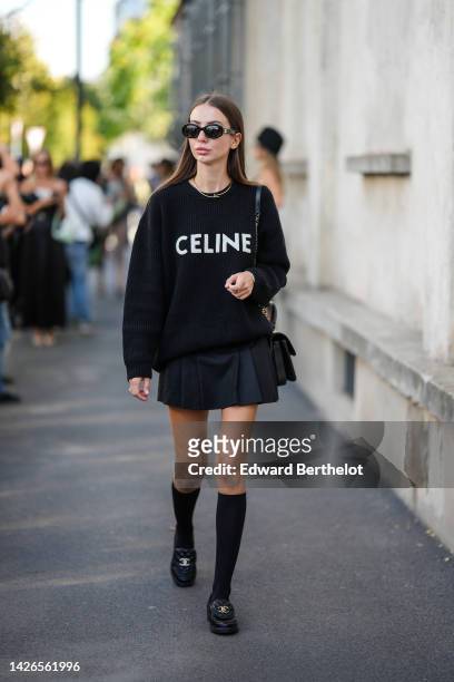 Guest wears black sunglasses, a gold Juste Un Clou necklace from Cartier, a black sweater from Celine, a black pleated short skirt, a black shiny...