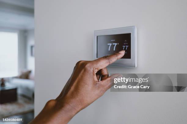 woman adjusts thermostat - thermostat fotografías e imágenes de stock