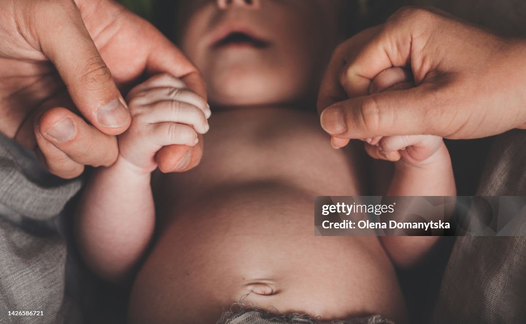 The parents are holding the hands of the newborn with their hands