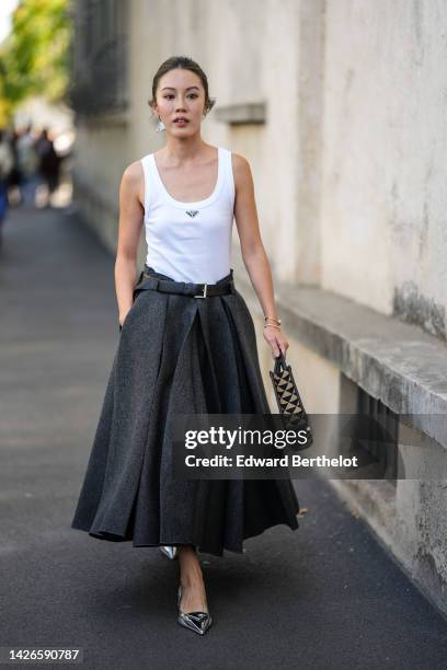 Guest wears a silver triangular pendant earring from Prada, a white tank-top from Prada, a dark gray wool long pleated skirt from Prada, a brown and...