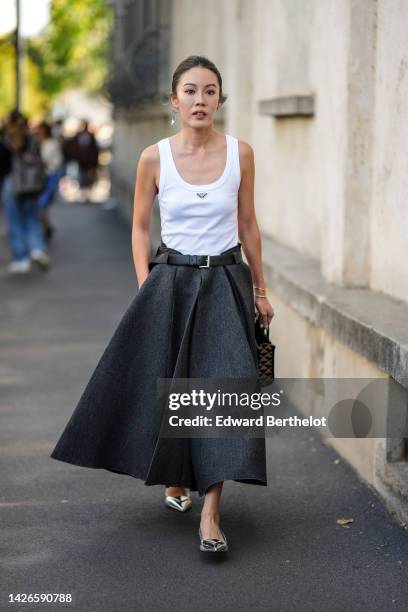 Guest wears a silver triangular pendant earring from Prada, a white tank-top from Prada, a dark gray wool long pleated skirt from Prada, a brown and...