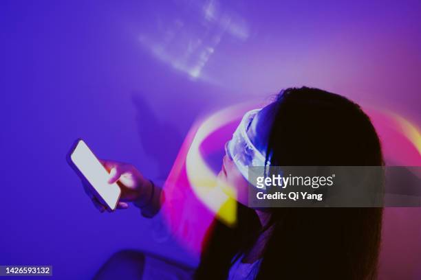 asian woman using smartphone surrounded by beams of light. metaverse and artificial intelligence - ai fotografías e imágenes de stock