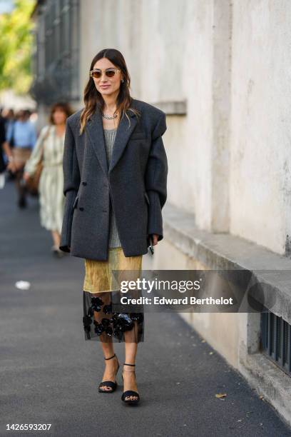 Guest wears beige sunglasses, silver and diamonds earrings, a large silver chain with gold details necklace, a gray ribbed wool long pullover, a...