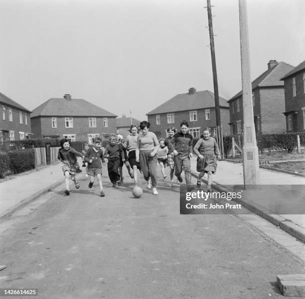 Wearing a track suit, 12 year-old footballer Margaret Wilde dribbles a ball down her street, chased by local children in Denton near Manchester,...