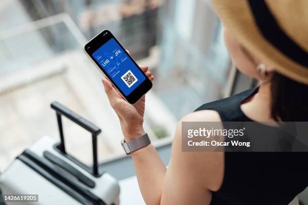 over the shoulder view of young woman checking in with electronic flight ticker on smart phone - phone screen at airport stockfoto's en -beelden