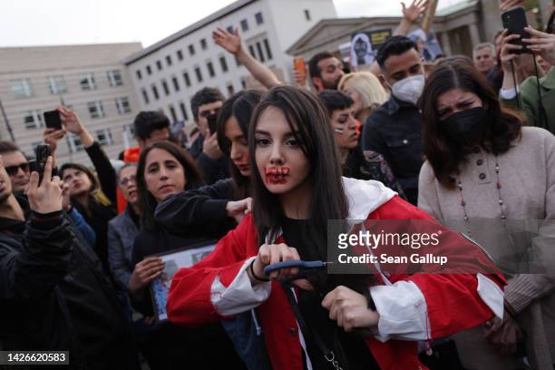 Young protester with red ink on her face that spells "HELP" cuts her hair with scissors as an act of solidarity with women in Iran during a...
