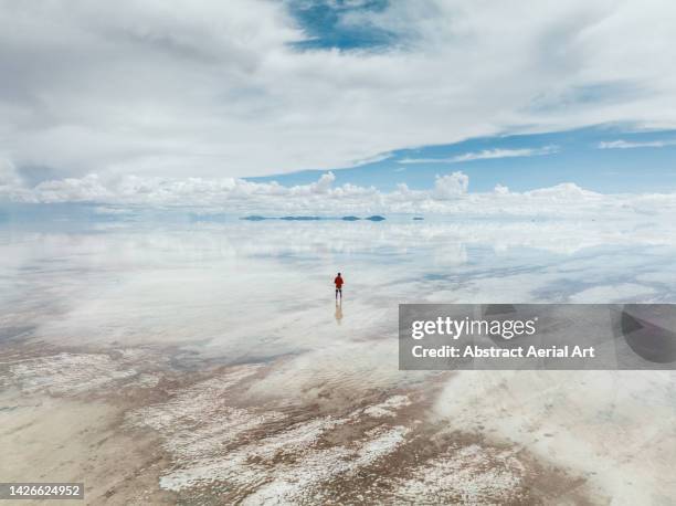 one man looking across a flooded salt pan during the day seen from a drone perspective, salar de uyuni, bolivia - salztonebene stock-fotos und bilder