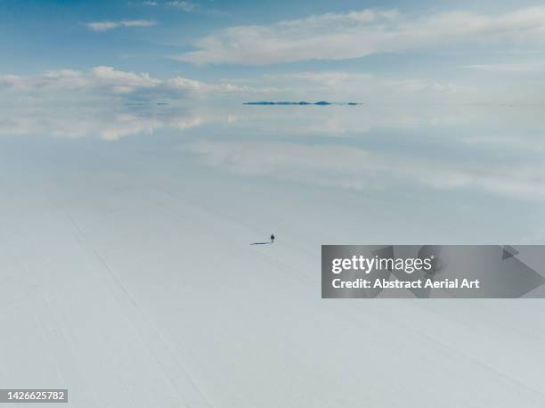 high angle drone image showing one person walking alone on a flooded salt pan, salar de uyuni, bolivia - uyuni stock pictures, royalty-free photos & images