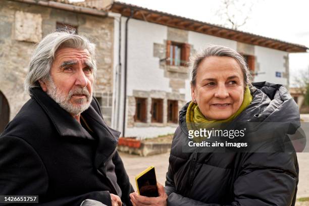 senior couple looking away, sitting on a public bench in an old town, enjoying a beautiful traditional parade. - marcha atrás imagens e fotografias de stock