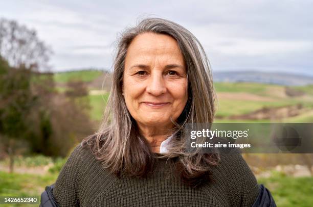 beautiful older woman with long gray hair enjoying a beautiful autumn day in the countryside, looking at the camera with a smile. - smile woman stock-fotos und bilder