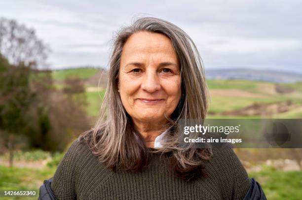 beautiful older woman with long gray hair enjoying a beautiful autumn day in the countryside, looking at the camera with a smile. - retratos fotografías e imágenes de stock