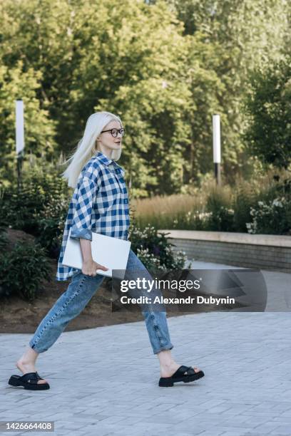 beautiful business woman walking on a city street with a laptop in her hands - businesswoman blond looking left foto e immagini stock