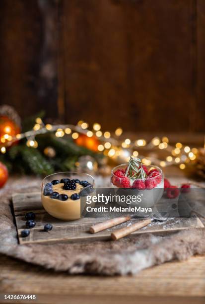 christmas dessert crème caramel and panna cotta with fresh berries in rustic wood kitchen and christmas lights - panna cotta stock pictures, royalty-free photos & images