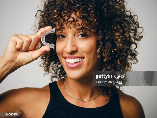 smiling woman holding an invisible teeth aligner - invisible braces stock pictures, royalty-free photos & images