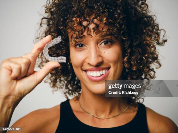 smiling woman holding an invisible teeth aligner - invisible braces stock pictures, royalty-free photos & images