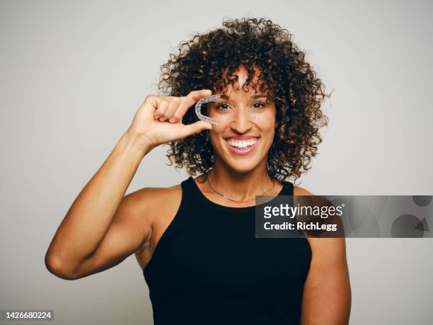 mujer sonriente sosteniendo un alineador de dientes invisible - orthodontics fotografías e imágenes de stock