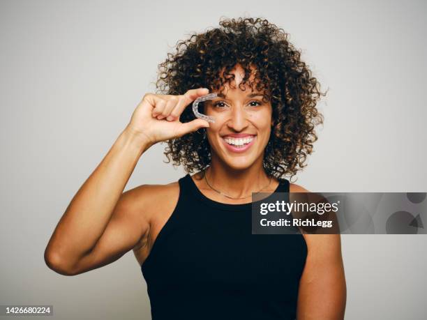 smiling woman holding an invisible teeth aligner - adult retainer stockfoto's en -beelden