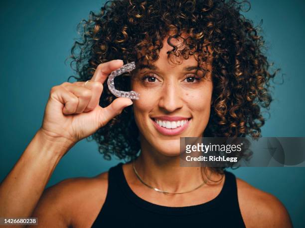 smiling woman holding an invisible teeth aligner - invisalign stockfoto's en -beelden