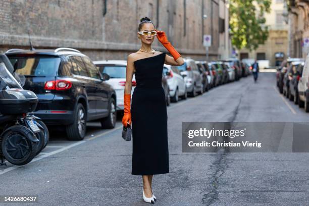 Anna Rosa Vitiello wears orange gloves, white sunglasses, black dress, black white heels, earrings, golden necklace outside Sportmax during the Milan...