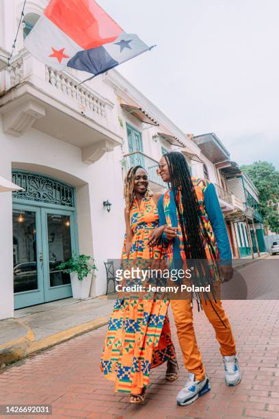 wide angle shot of a fashionable afro-descendant tourist couple walking together in the street under a panamanian flag in panama city - panama city panama stockfoto's en -beelden