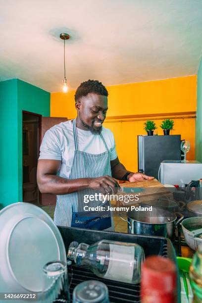 portrait of a cheerful black male chef adding ingredients to a stew pot in his kitchen in panama city, panama - panama food stock pictures, royalty-free photos & images