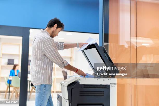 man working in office making copies of reports for meeting in board room with colleagues, modern office. - by the photocopier stockfoto's en -beelden