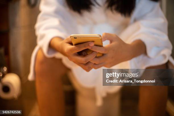 woman holding a phone while using the toilet, mock up phone white screen display in hand - men taking a dump stockfoto's en -beelden