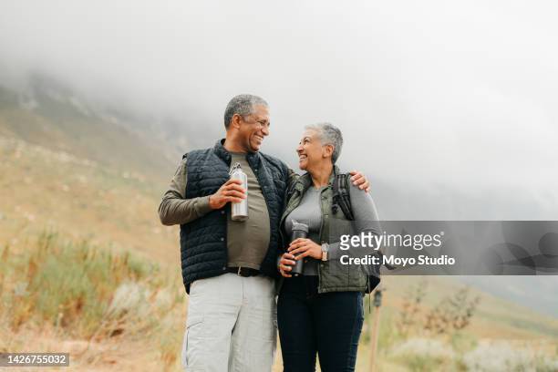 senior couple hiking in the mountains in nature, walking for fitness on holiday in mountain and exercise during vacation in the countryside together. happy latino man and woman on walk for health - retired couple stockfoto's en -beelden