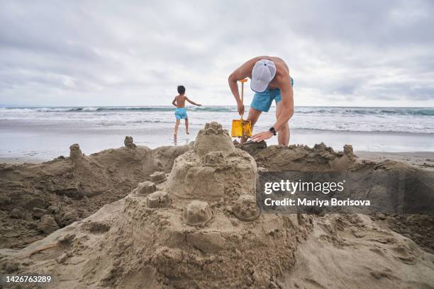 a family with two children is building a sand castle on the sea in cloudy weather. - sandburg stock-fotos und bilder