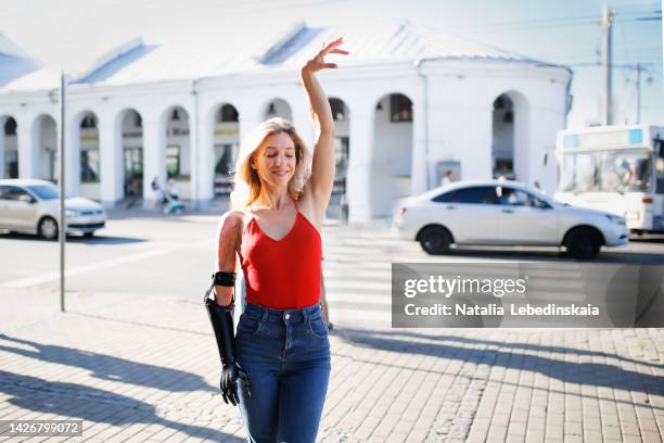 pretty woman in red on sidewalk on street in small town in summer. joy of life. - artificial arm stock pictures, royalty-free photos & images