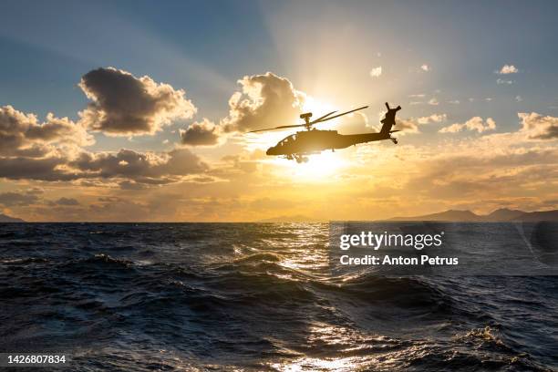 military helicopter over the sea at sunset - apache helicopter in action stockfoto's en -beelden