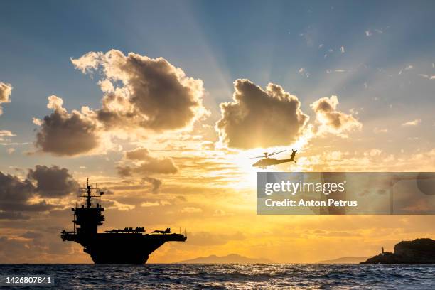 aircraft carrier and helicopter at sunset in the sea - industria della difesa foto e immagini stock