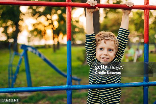 a boy looks directly into the camera while playing on the jungle gym in the park - monkey bars imagens e fotografias de stock
