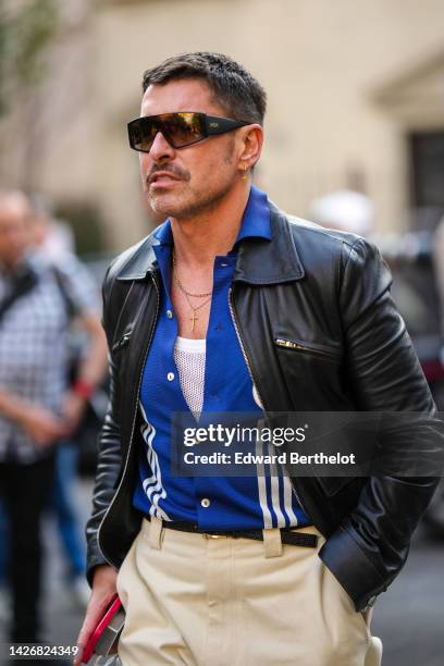 Alex Badia wears black sunglasses from Mom, a white tank-top, a navy blue with white striped print pattern polo shirt, a black shiny leather jacket,...