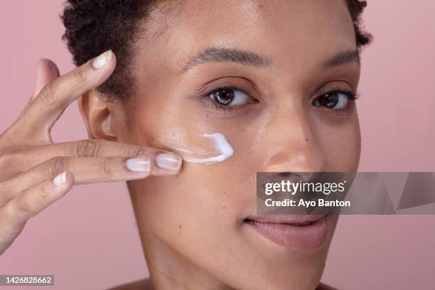 studio portrait of woman applying cream on face - 乳液 ストックフォトと画像