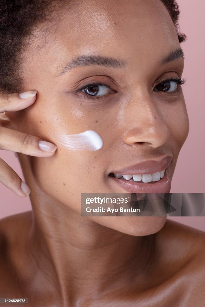 Studio portrait of smiling woman applying cream on face