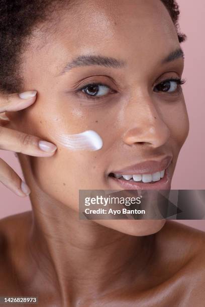 studio portrait of smiling woman applying cream on face - cream for face stock pictures, royalty-free photos & images