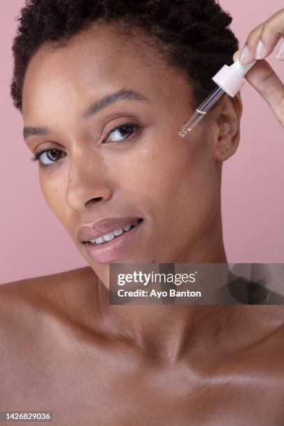 studio portrait of woman dropping cosmetic oil on face - face oil stock pictures, royalty-free photos & images