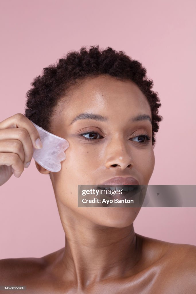 Studio portrait of woman massaging face with rose quartz guasha