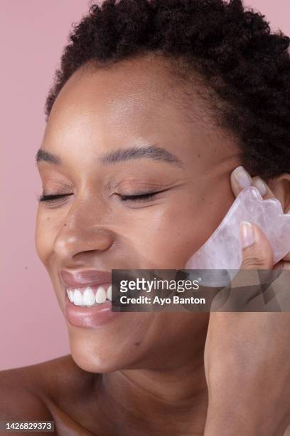 studio shot of smiling woman massaging face with rose quartz guasha - spooning stock pictures, royalty-free photos & images