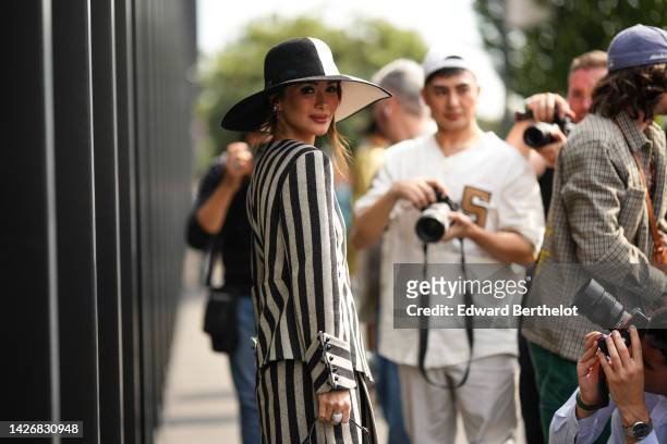Heart Evangelista wears a half black and half white felt hat from Gucci, silver and pink earrings, a pale gray and black striped print pattern jacket...