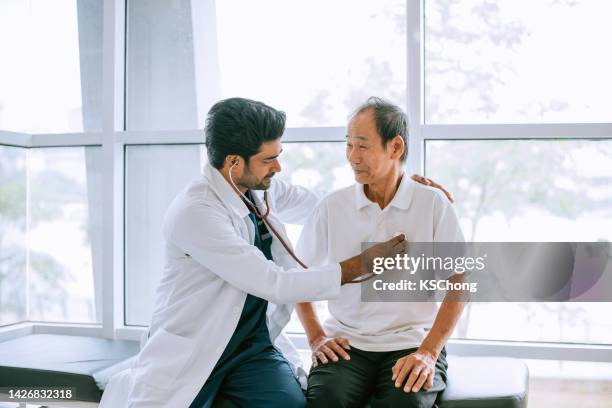 aufnahme eines arztes, der einen patienten während einer konsultation in einem krankenhaus mit einem stethoskop untersucht - adult patient with doctor and stethoscope stock-fotos und bilder