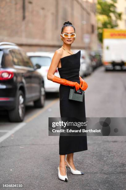 Anna Rosa Vitiello wears white and orange sunglasses, gold earrings, a gold necklace, a black square neck / shoulder-off / midi tube dress, orange...