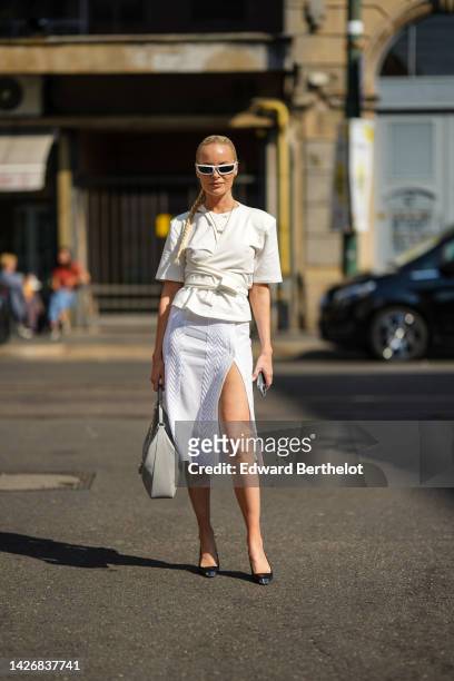 Thora Valdimars wears white sunglasses from Prada, gold earrings, gold chain pendant necklaces, a white latte short sleeves / belted t-shirt, a white...