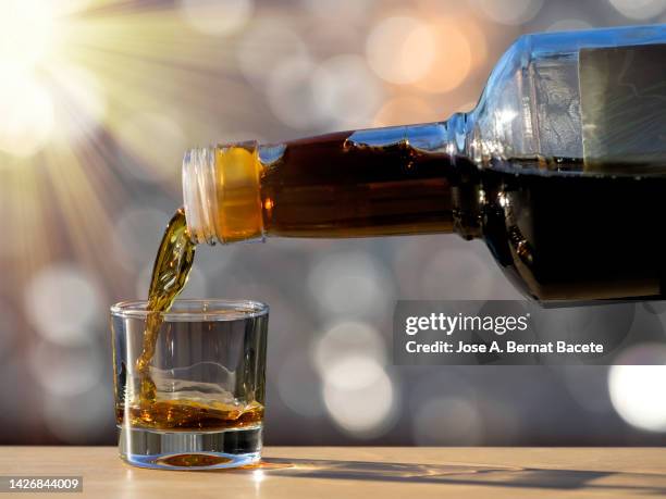 filling a shot glass with a liquor bottle lit by sunlight. - likör stock-fotos und bilder