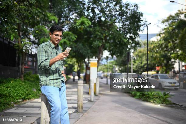 man using his mobile phone while standing on a city street - mumbai daily life stock pictures, royalty-free photos & images